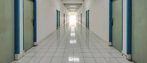 A long, narrow hallway with blue-framed doors on both sides, leading to individual rooms. The floor is tiled, and the hallway is well-lit with overhead lights.