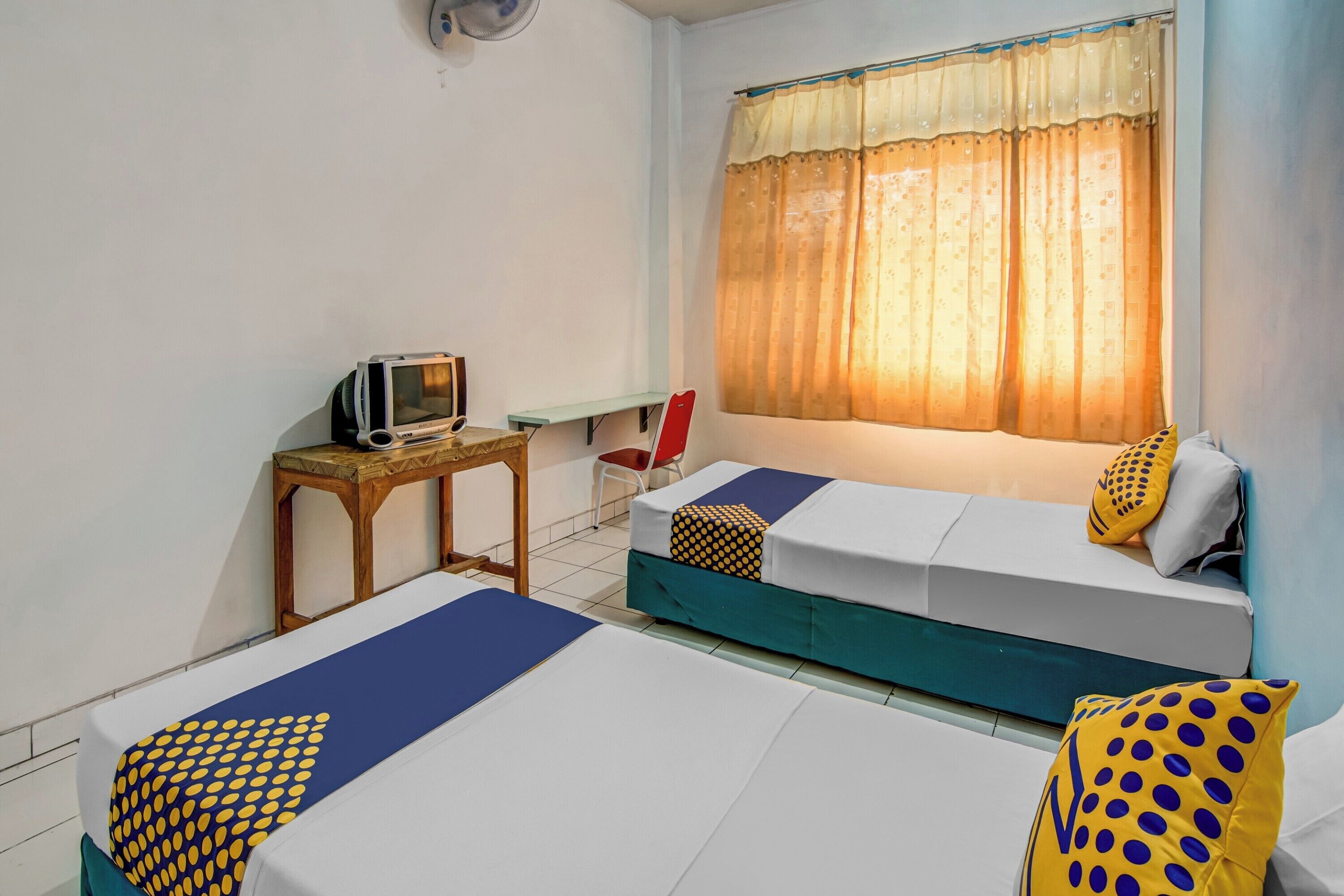 A room with two beds, a TV, a small table, and a window with curtains.