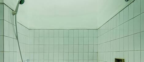 A small, tiled bathroom with a squat toilet, a showerhead, and a light fixture on the ceiling.