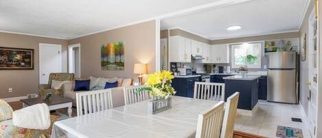 Una cocina moderna con armarios blancos, un refrigerador de acero inoxidable y un comedor con mesa y sillas blancas.