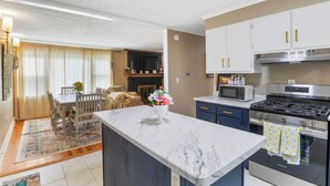 Eine moderne Küche mit Kochinsel, ein Essbereich mit Tisch und Stühlen sowie ein Wohnzimmer mit Kamin.