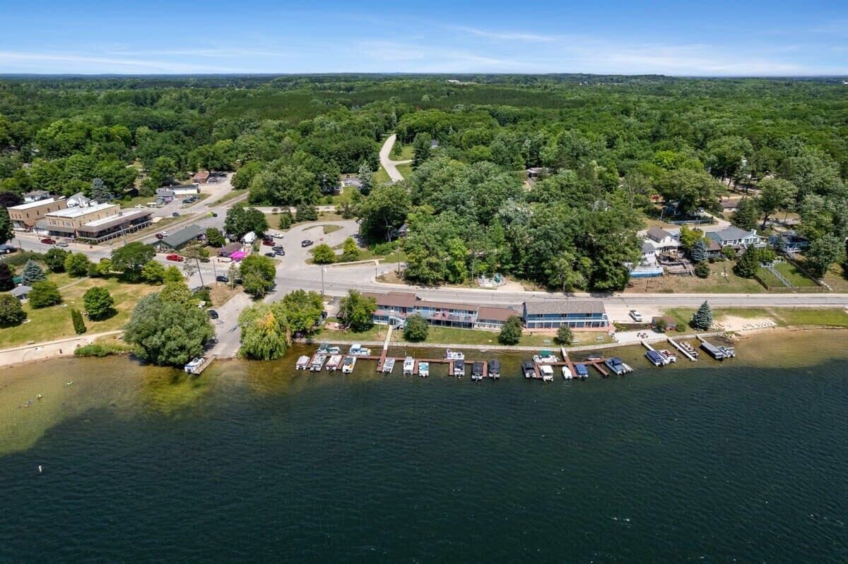 An aerial view of a lakeside property with a parking lot, buildings, and a road.