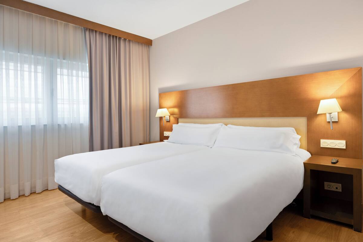 A double bed with white linens, two bedside lamps, a wooden headboard, and a nightstand with a remote control.