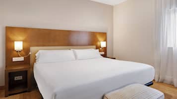 A hotel room with a large bed, two bedside tables with lamps, a wooden headboard, and a window with curtains.