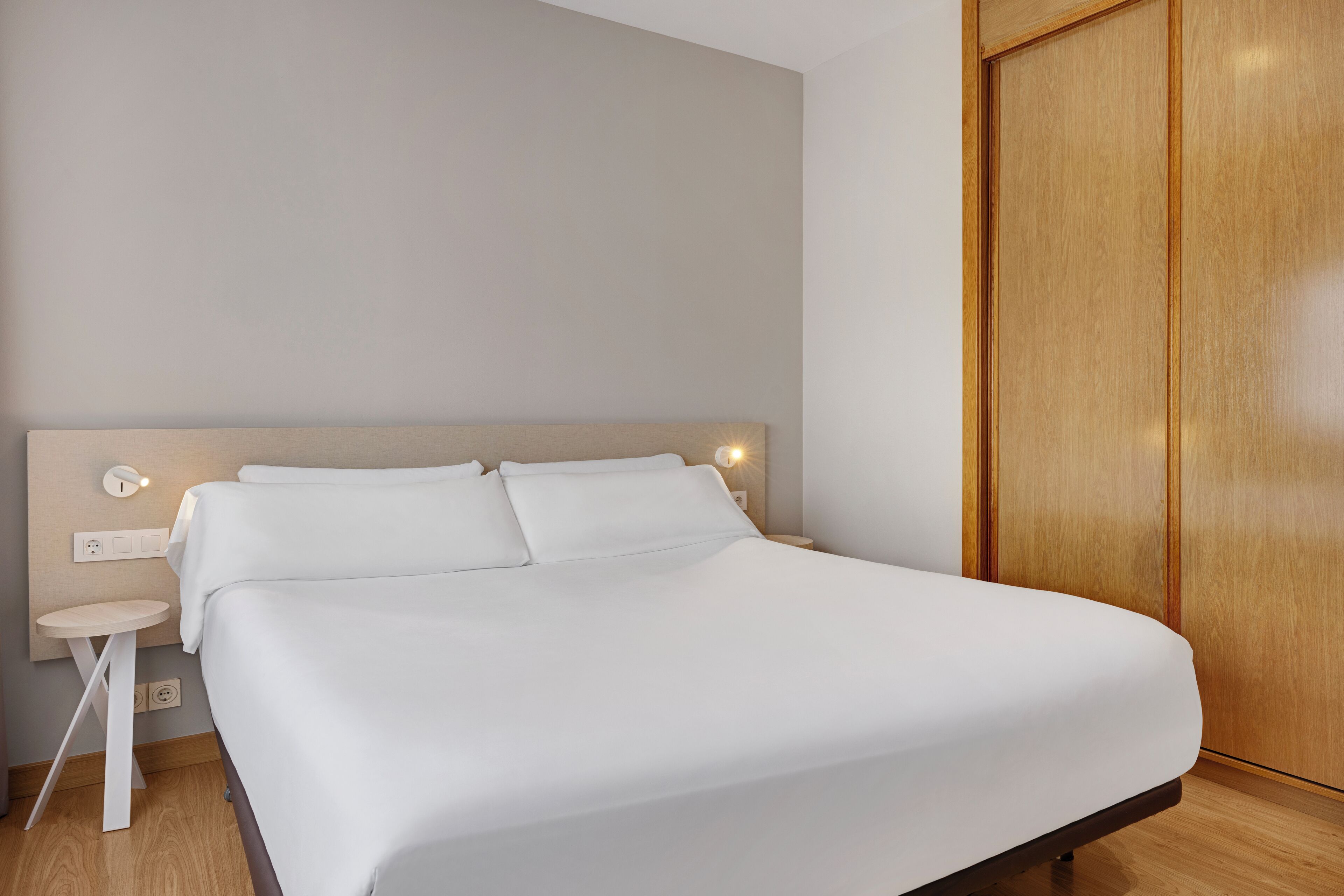 Une chambre d’hôtel moderne avec un grand lit, une table de chevet et une armoire en bois.