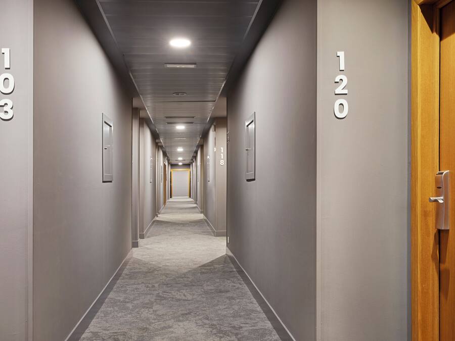 Pasillo de hotel con puertas numeradas, pisos alfombrados e iluminación empotrada.