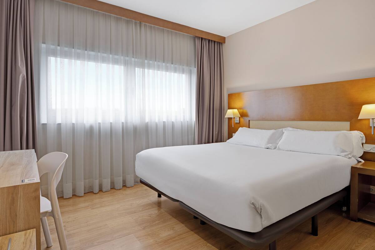 A hotel room with a large bed, a desk, and a chair.