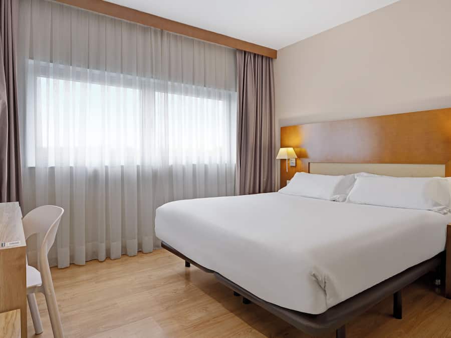 A hotel room with a large bed, a desk, and a chair.