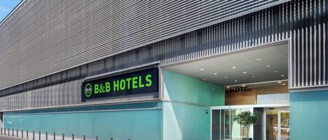 Un hotel tipo B&B moderno con un letrero llamativo, un acceso cubierto y fachada de vidrio.