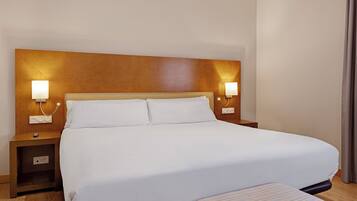 Una habitación de hotel con una cama grande, lámparas de noche, una mesita de noche y un cabecero de madera.