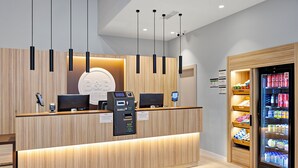 A reception area with a wooden reception desk, two monitors, a self-service kiosk, and a refrigerated display case. - B&B Hotel Logroño Las Cañas (Viana)