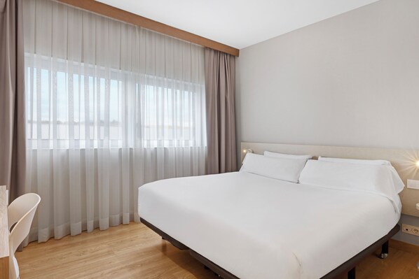 A modern hotel room with a large bed, a bedside table, a chair, and a window with sheer curtains. - B&B Hotel Logroño Las Cañas (Viana)