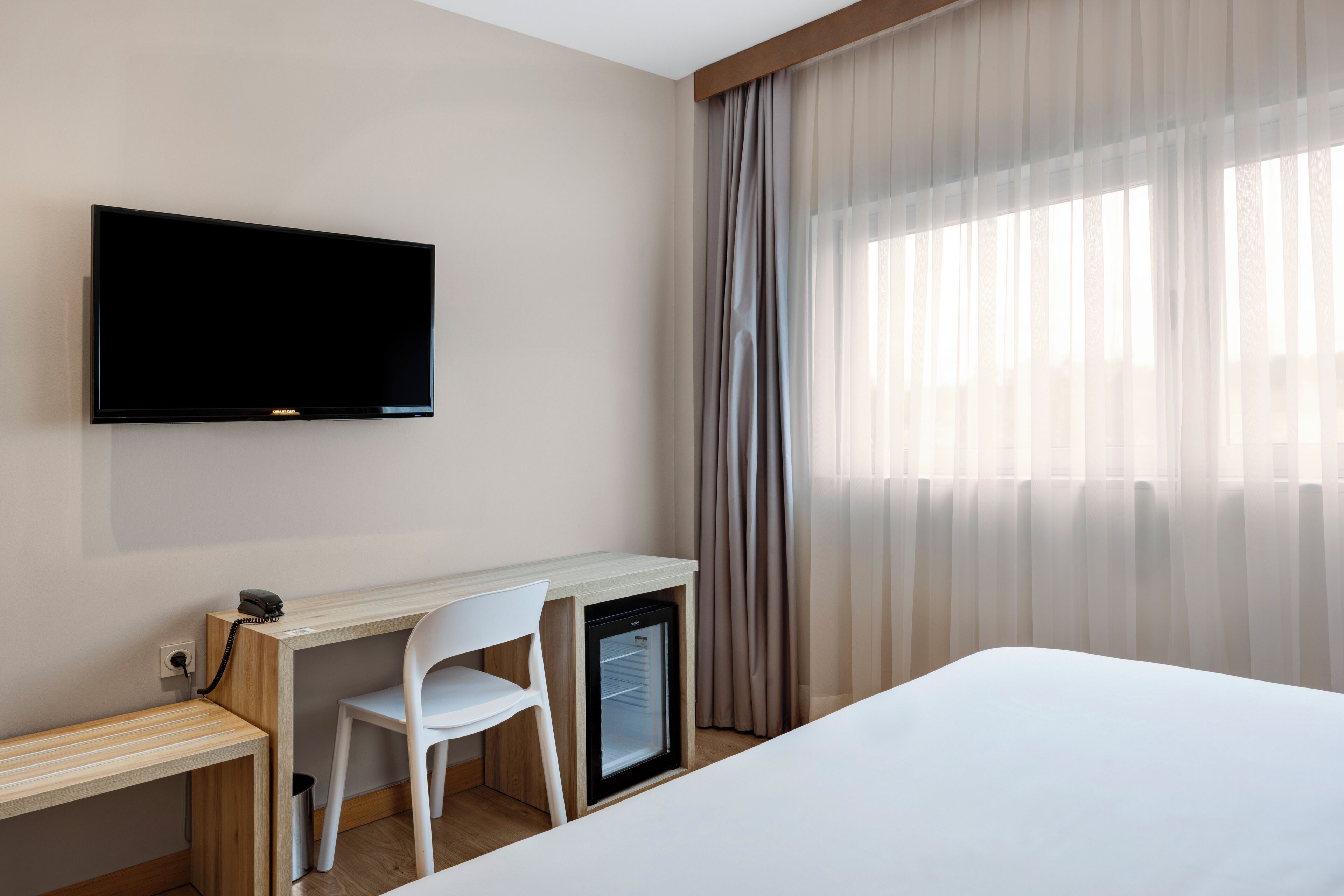 Una habitación de hotel con cama, escritorio con silla, televisor y refrigerador pequeño.