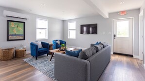 Una sala de estar moderna con un sofá modular gris, sillones azules, una mesa de centro de madera, cestas de mimbre y un cartel enmarcado en la pared.
