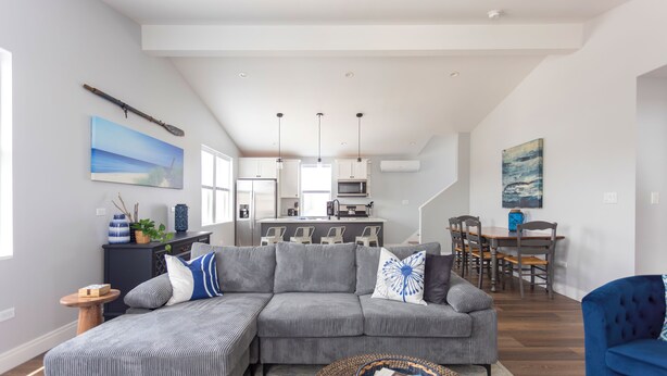 Un salón amplio con un sofá seccional gris, un sillón azul y un comedor con mesa y sillas.
