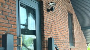 A brick exterior with a dark gray door, a small window, and a black metal handrail. - Stork's nest apartment (Steinburg)