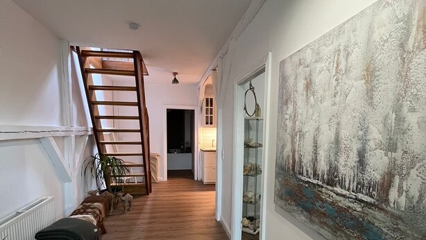 A hallway with wooden flooring, a staircase, a radiator, and a large painting on the wall. - Stork's nest apartment (Steinburg)