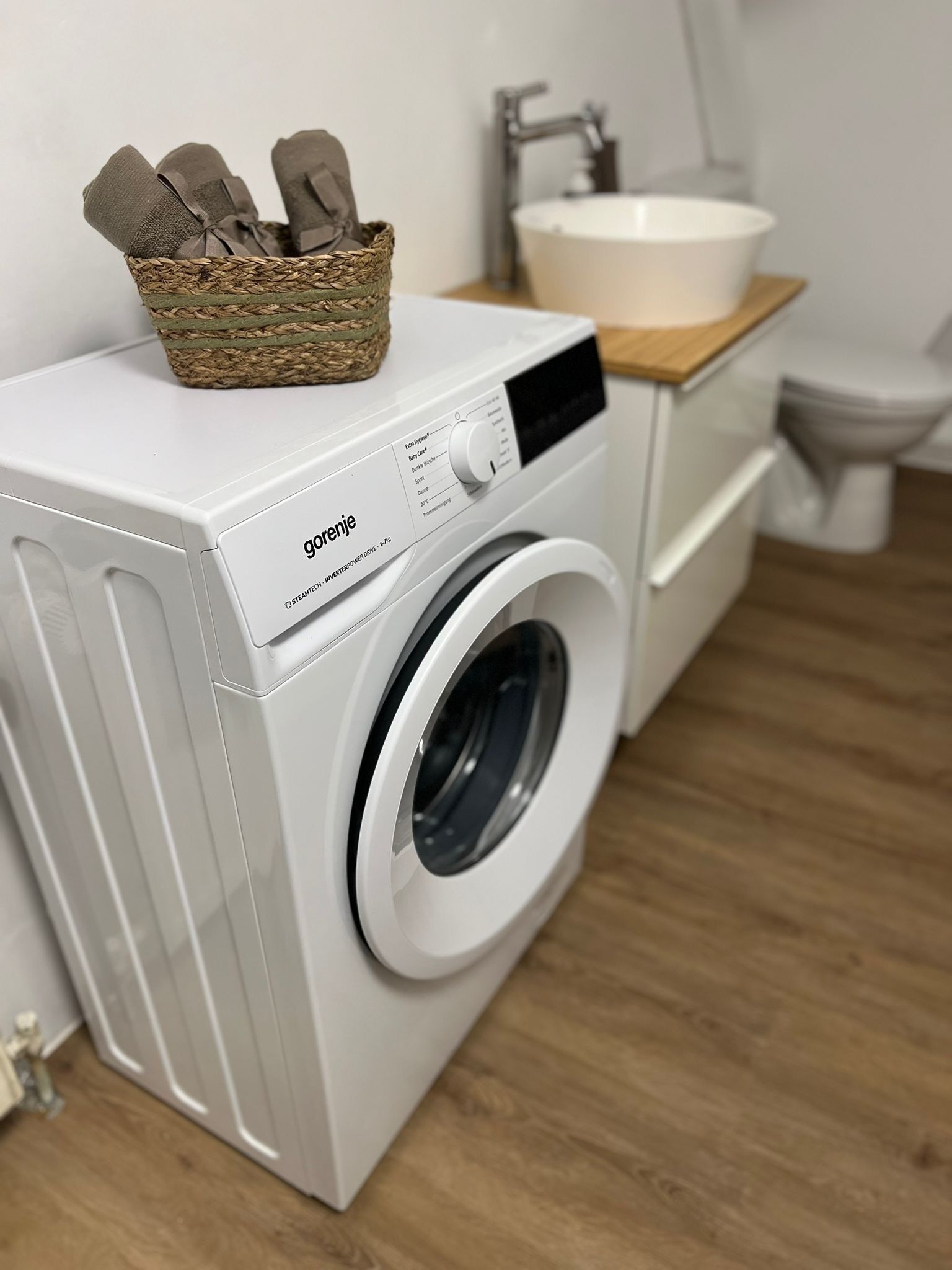 Un lave-linge moderne et compact, doté d’un panneau de commande et surmonté d’un panier rempli de vêtements pliés.