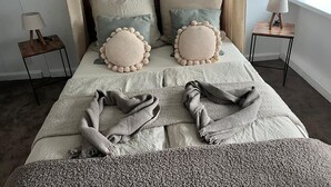 A neatly made bed with two decorative pillows, a bedside table with a lamp, and a window with curtains. - Stork's nest apartment (Steinburg)