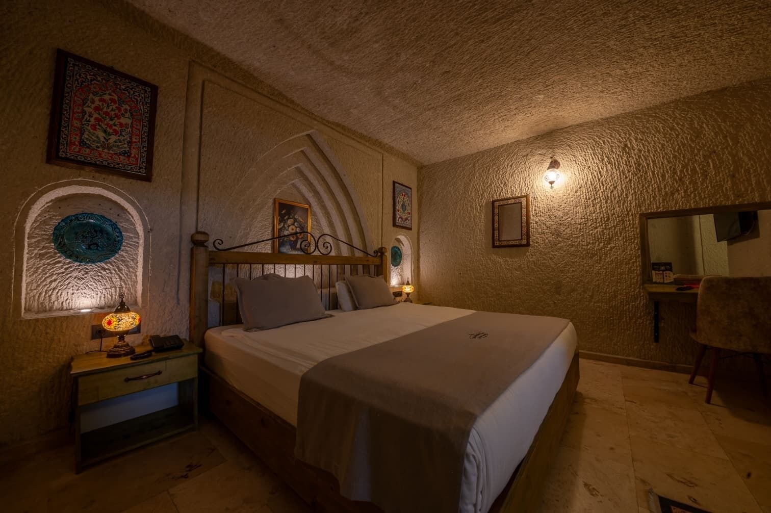 Une chambre à coucher comprenant un lit, une table de chevet, une lampe, un miroir et un mur orné d’un motif texturé.