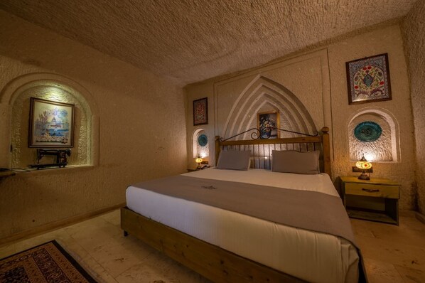 A bedroom with a wooden bed, a nightstand with a lamp, and a wall-mounted painting.