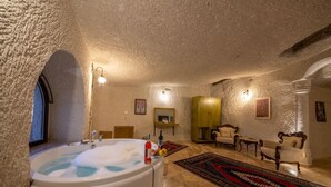 A room with a large bathtub, a wooden cabinet, a sofa, and a patterned rug. - Majestic Cave House (Nevsehir)