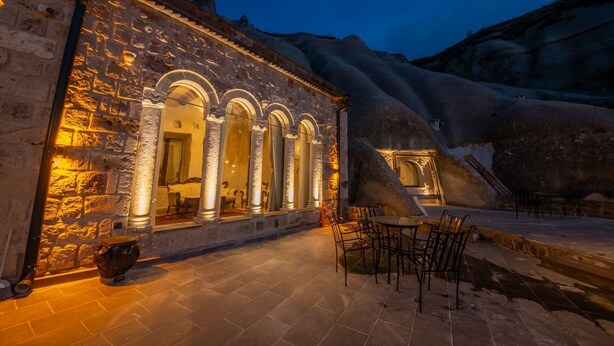 A stone building with arched windows and a patio area with chairs. - Majestic Cave House (Nevsehir)