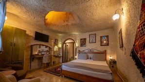 A cozy bedroom with a wooden bed, a desk, and a chair, featuring stone walls and a ceiling cave. - Majestic Cave House (Nevsehir)