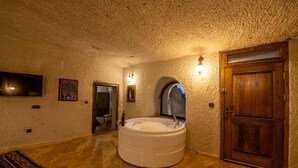 A room with a large bathtub, a wooden door, and a textured ceiling. - Majestic Cave House (Nevsehir)