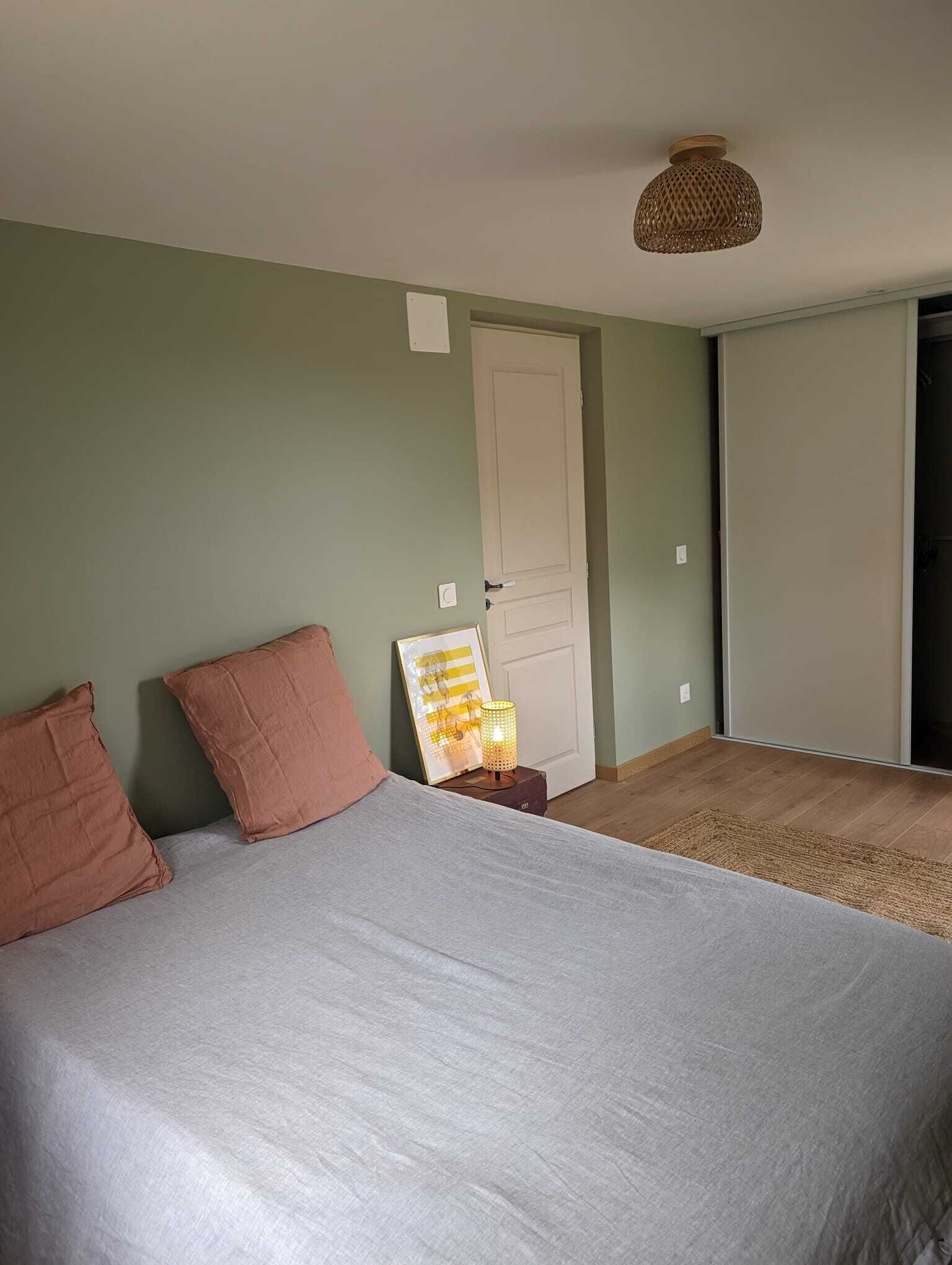 Une chambre à coucher avec un lit, deux oreillers, une table de chevet avec une lampe, une porte et une vue sur un couloir.