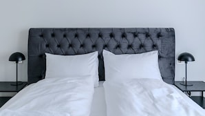 Una cama con cabecera capitonada, dos almohadas blancas y dos mesitas de noche negras con lámparas.