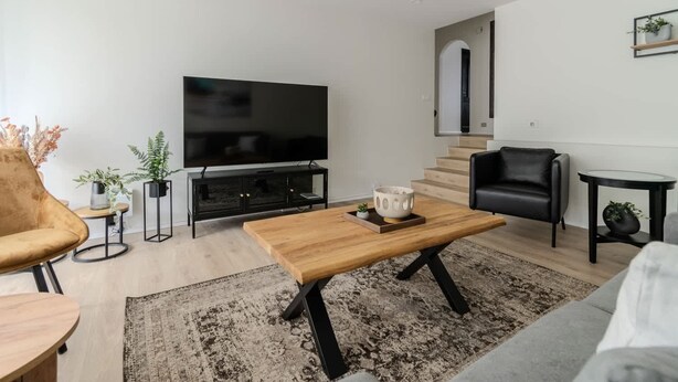 Una sala de estar moderna con un televisor de pantalla plana, una mesa de centro de madera, un sofá de cuero negro y una escalera que lleva a otro nivel.