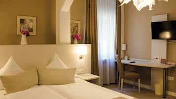 A hotel room with a bed, a desk, a chair, a TV, and a window with curtains.