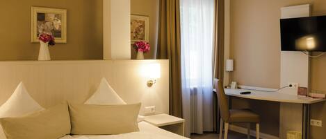 A hotel room with a bed, a desk, a chair, a TV, and a window with curtains.