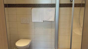 A bathroom with a toilet, a shower with a glass door, and a towel rack with two white towels.