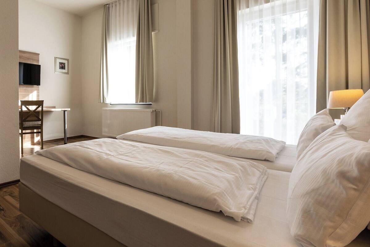 Een hotelkamer met twee bedden, een bureau, een stoel en een raam met gordijnen.