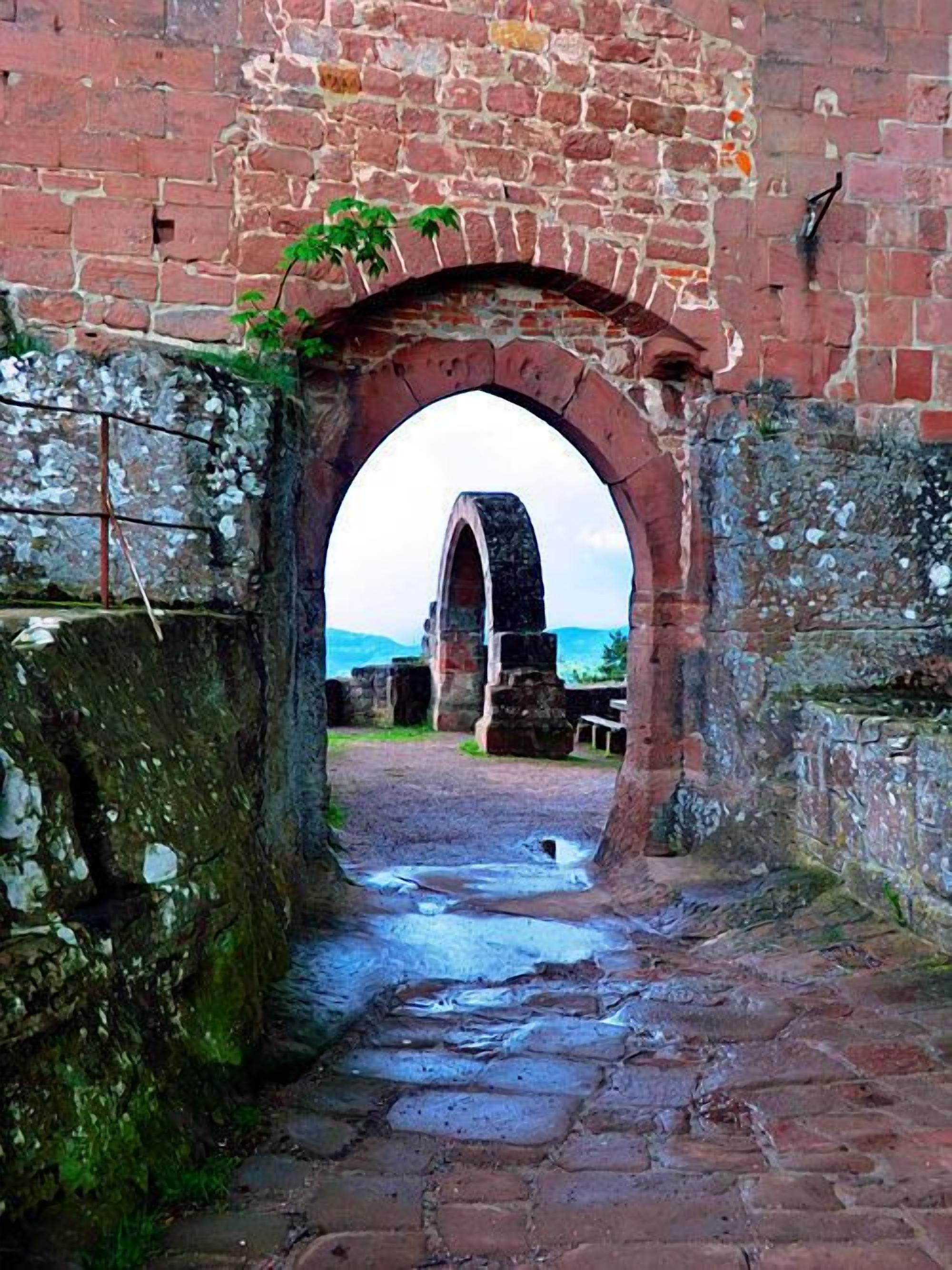 An arched stone gateway leading to a courtyard with a stone bench and a view of distant hills.