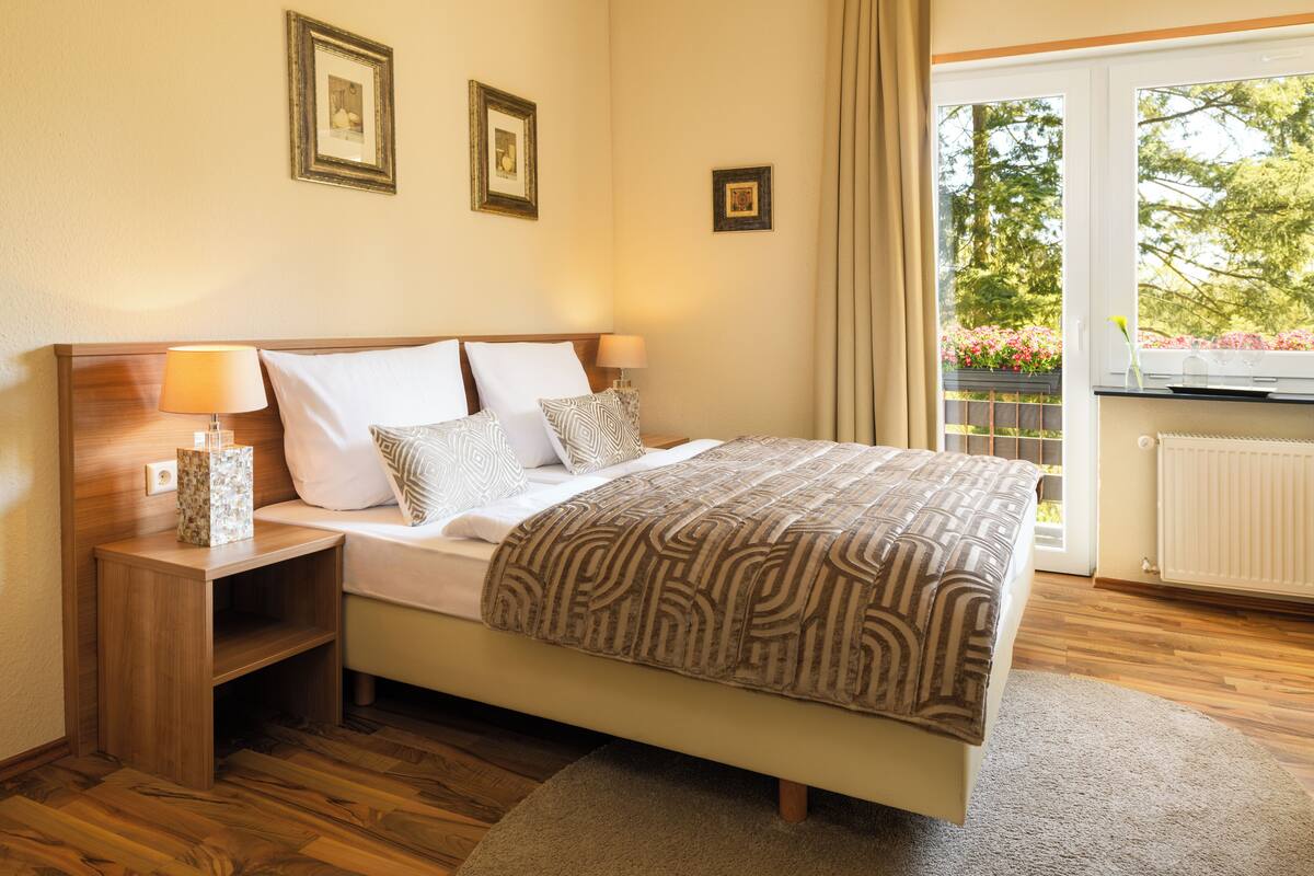 Een netjes ingerichte slaapkamer met een bed, nachtkastjes en een raam met uitzicht op groen.