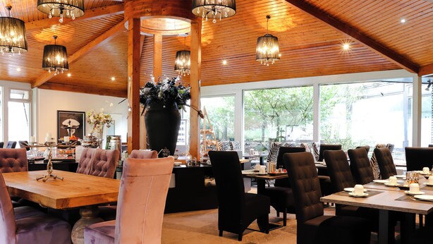A spacious dining area with high ceilings and wooden beams, featuring a large wooden table and multiple upholstered chairs.