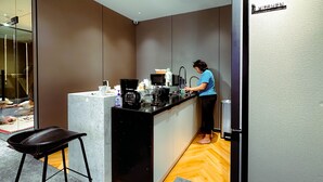A compact kitchen with a marble countertop, a coffee maker, and a person preparing food. - UBPOD capsule hotel in Mongolia (Ulaanbaatar)