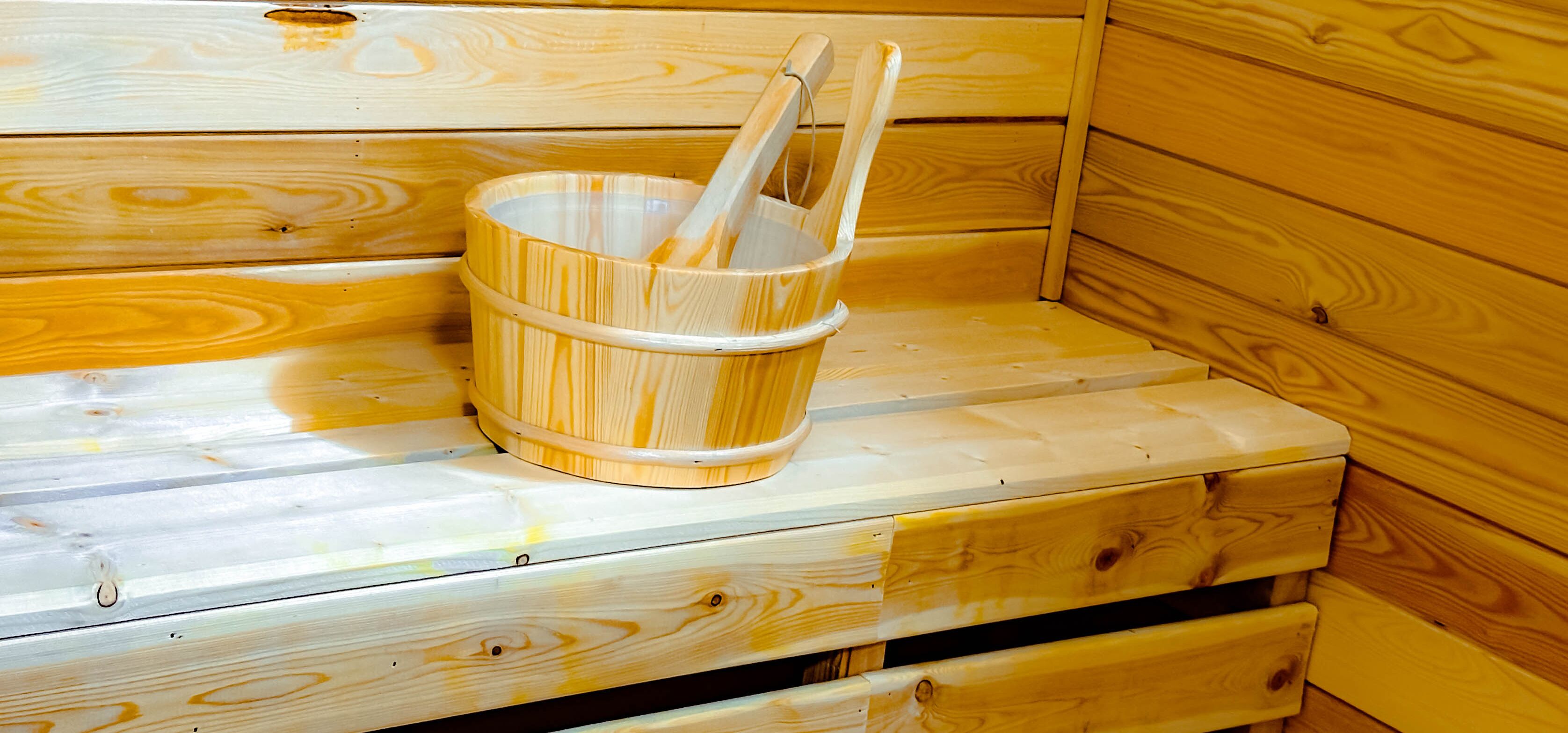 Banco de sauna de madera con un cubo de madera y dos palos de madera.