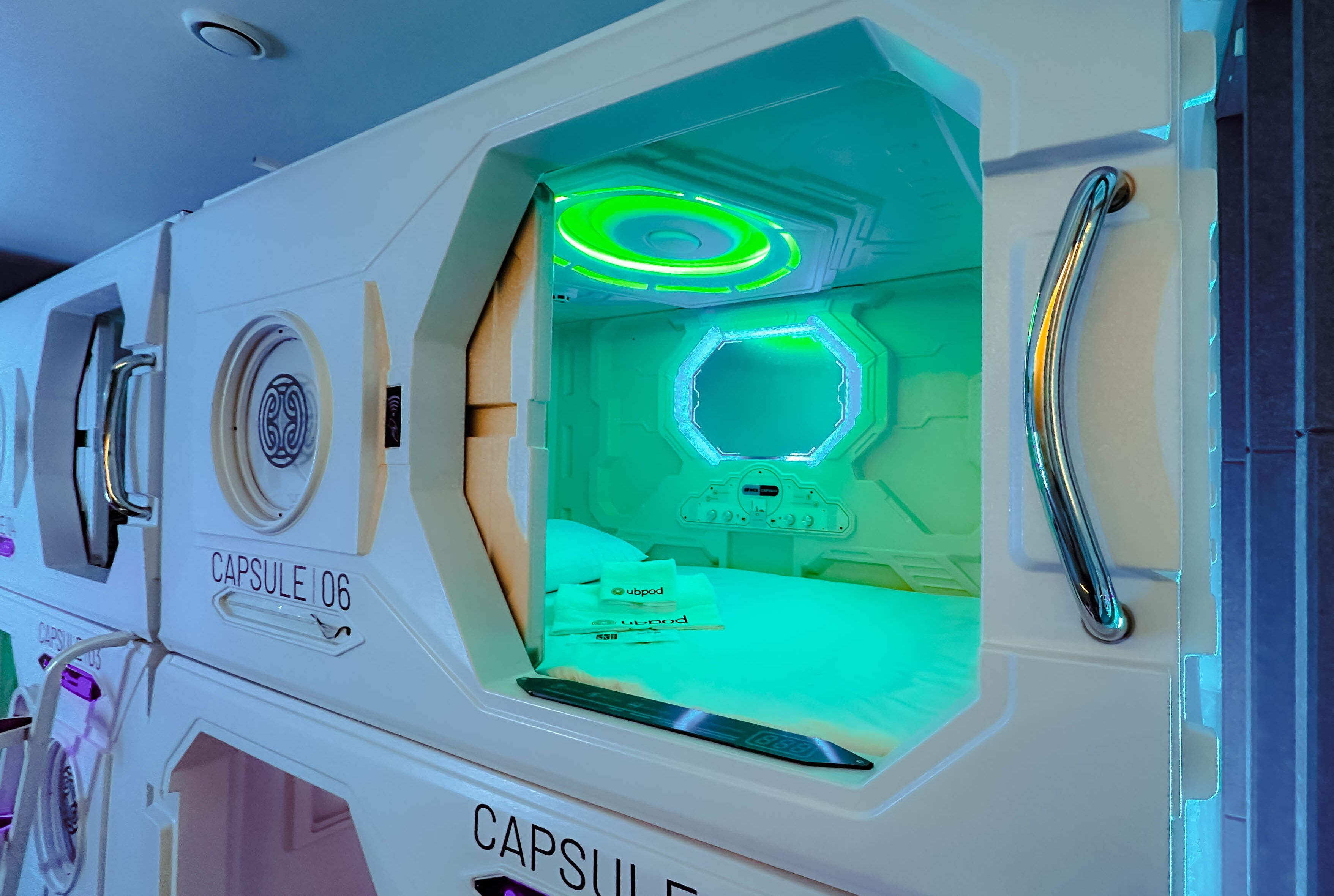 Interior de un hotel cápsula con una habitación iluminada en verde, un asa y una etiqueta que dice 'Capsule106'.