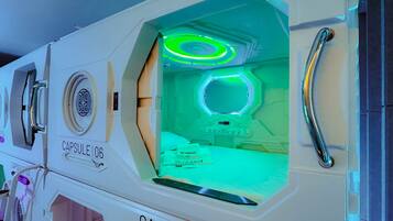 Interior de un hotel cápsula con una habitación iluminada en verde, un asa y una etiqueta que dice 'Capsule106'.