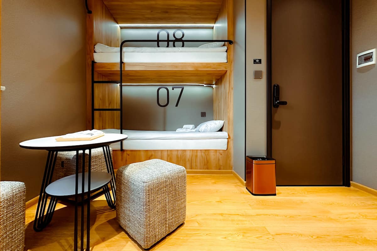 A compact room with bunk beds labeled 07 and 08, a small round table, two cushioned seating areas, and a door with a handle.
