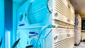 A room with a large, white, futuristic-looking capsule labeled "Capsule 107" and a smaller "Capsule 108". - UBPOD capsule hotel in Mongolia (Ulaanbaatar)
