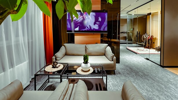 A modern living room with a beige sofa, a coffee table with decorative items, and a television displaying a program. - UBPOD capsule hotel in Mongolia (Ulaanbaatar)