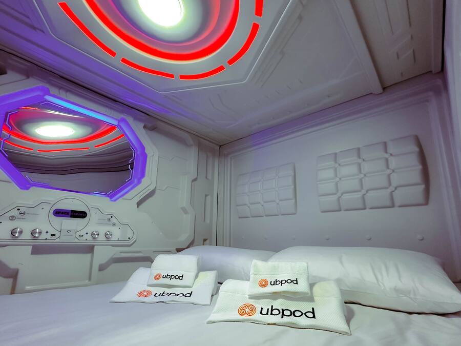 A modern room with a bed, a control panel, and a ceiling light fixture.