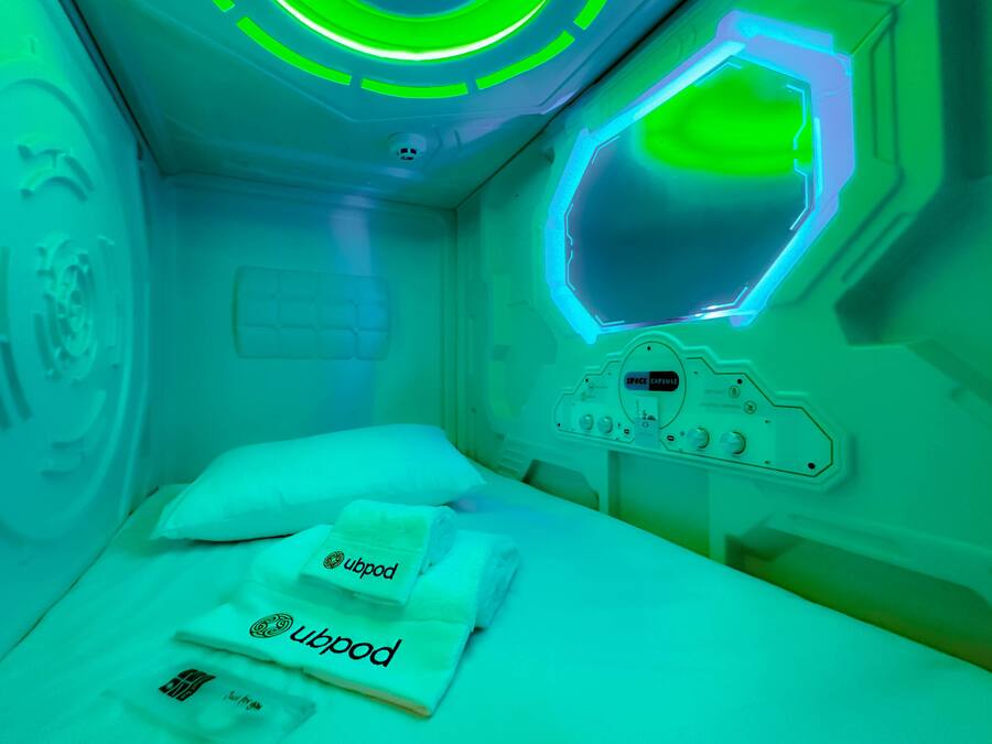 A medical treatment room with a bed, a control panel, and a green-lit ceiling.