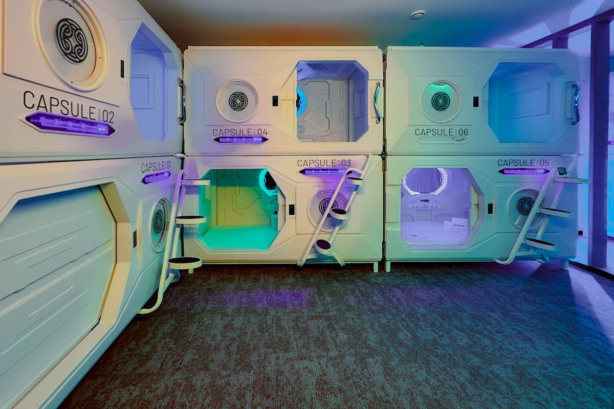 A row of capsule-style hotel rooms with individual names and a central control panel.