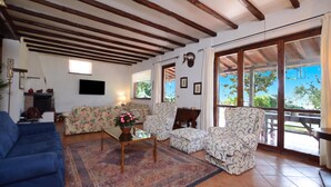 A living room with a sofa, armchair, and coffee table, a TV, and a large window with a view. - Casale Pontarello (Vetralla)